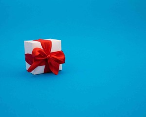 White gift box with red ribbon on blue background.