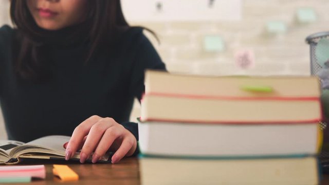 Young Asian female college student concentrating on reading book at the table preparing for examination