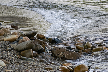 Large and smooth stones in the coastal waves of salty sea water. The coast of the black sea foams and roars, beating against a huge pebble, illuminated by sunlight