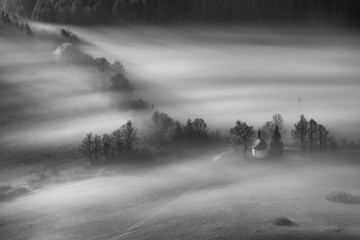 Chapel surrounded by trees in autumn fog