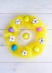 Easter wreath of sisal, colored eggs, cotton and feathers on a wooden background. Vertical orientation, top view.