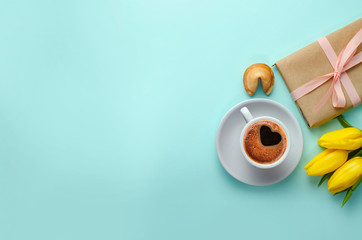 Morning coffee with tulips flowers, fortune cookies and gifts on blue background. Spring concept. 