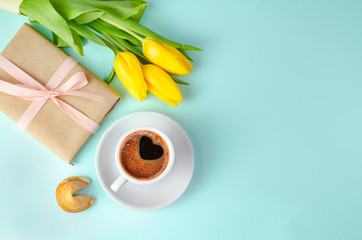 Morning coffee with tulips flowers, fortune cookies and gifts on blue background. Spring concept. 