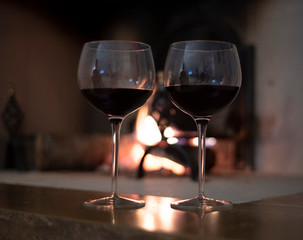 Two glasses of red wine in front of a warm fire