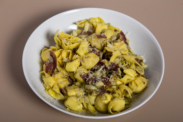 Baked cheese tortellini or belly button pasta with Iberian ham on wooden background.