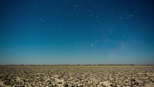 Linear Timelapse of a moonlight landscape over a vast, empty desert Salt Pan in Botswana, Baines Baobab plains, tilting up to Milky Way after moon set.