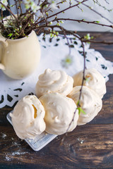 Homemade meringue cookies on rustic wooden table, homemade white napkin and spring tree branches in vase. Beautiful dessert, tasty breakfast, natural light, selective focus, copy space, flat lay.