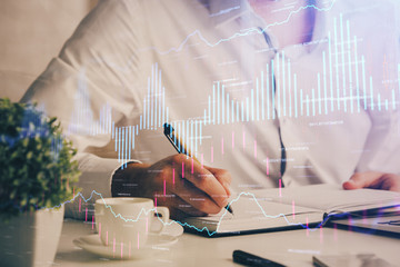 Double exposure of man's hands writing notes of stock market with forex chart.