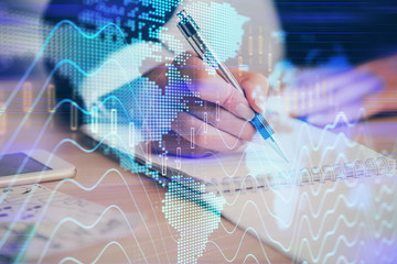 A woman hands writing information about stock market in notepad. Forex chart holograms in front. Concept of research. Multi exposure