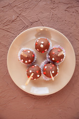 Chocolate candies covered with pink and red hearts on a stick lie on a white plate
