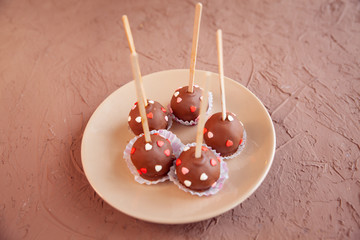 Chocolate candies covered with pink and red hearts on a stick lie on a white plate