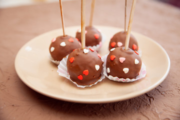 Chocolate candies covered with pink and red hearts on a stick lie on a white plate