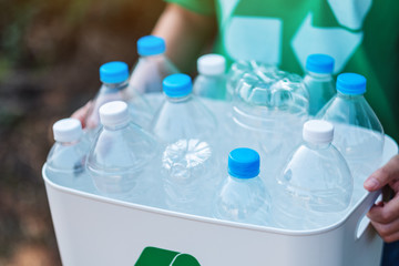 A woman collecting garbage and holding a recycle bin with plastic bottles in the outdoors