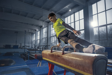 Control. Little male gymnast training in gym, flexible and active. Caucasian little boy, athlete in sportswear practicing in exercises for strength, balance. Movement, action, motion, dynamic concept.