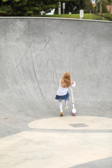 Obraz na płótnie Canvas Little girl riding scooter at skate park 