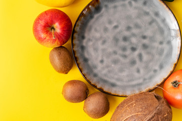 Ceramic grey empty plate top view on yellow background. Many fruits and vegetables. Vegan food