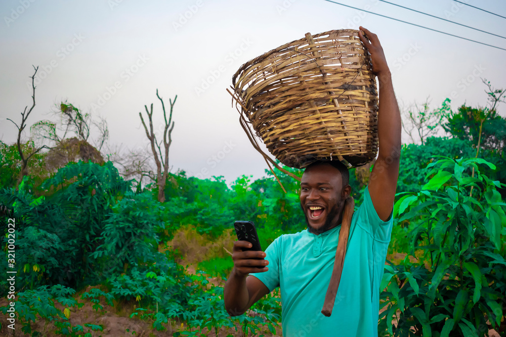 Wall mural young black happy farmer carrying a basket of his farm produce on his head