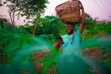 young black happy farmer carrying a basket of his farm produce on his head