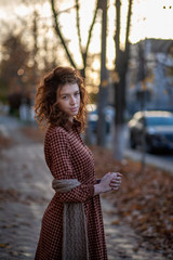 Dreaming young woman with spectacular curly red ginger hair looking at camera posing outdoor in...