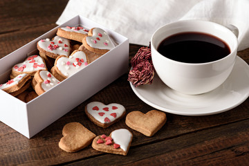 cookies hearts with icing in white box and Cup of red tea and rose on wooden background
