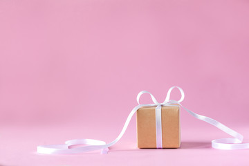 Gift or present box with white ribbon on pink background. Holiday greeting card.