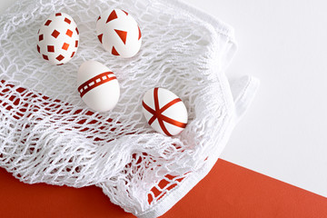 four white Easter eggs with red geometric pattern on white mesh eco bag on red and white background