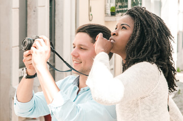 Excited mix raced couple of tourists taking pictures of landmarks. Young Caucasian guy and black girl walking in old city. Sightseeing concept