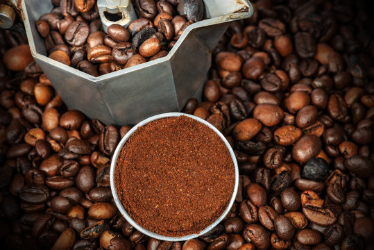 Close-up of an open Italian coffee maker with ground coffee in the metal filter, on many roasted coffee beans