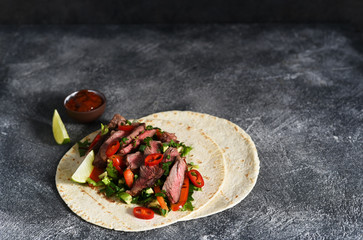 Classic Mexican dish - corn tortilla with vegetables and beef on a kitchen stone table.