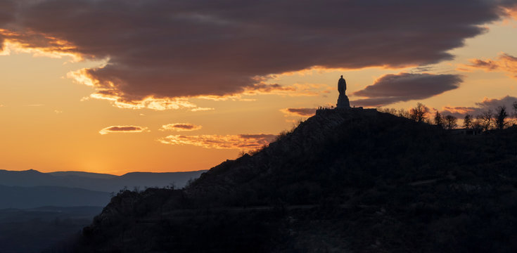 Monument to Alyosha in Plovdiv, Bulgaria. Colorful panoramic picture with the silhouette of the monument to Alyosha, standing on a hill against a golden sunset sky and dramatic black clouds.