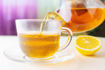 Hot herbal tea from a teapot is poured into a transparent cup. Nearby lies a lemon. The concept of healthy organic drinks.