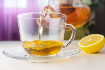 Hot herbal tea from a teapot is poured into a transparent cup. Nearby lies a lemon. The concept of healthy organic drinks.