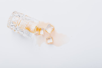 overturned glass with whiskey on a white background, ice cubes fell out of a glass