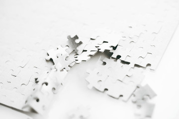 White assembled puzzle that is broken into small parts in one place. A metaphor for the destruction or disintegration of the whole.