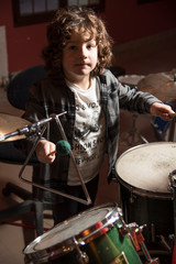 Fototapeta na wymiar Curly-haired boy and gray shirt of shirtmakers playing drums like a pro. Fun and passion playing music