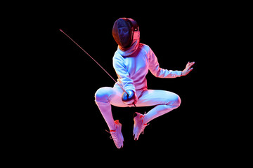 Movement. Teen girl in fencing costume with sword in hand isolated on black background, neon light....