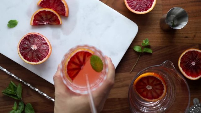 Hand serves refreshing cold summer cocktail with blood orange and mint with glass tube