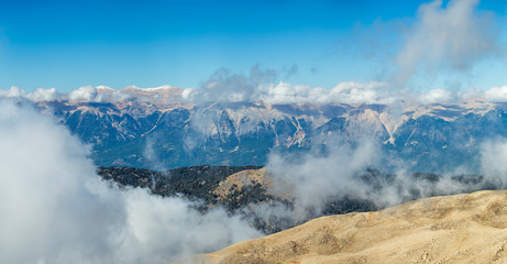 Panoramic aerial view horizontal photography of amazing cloudy peaks of high mountains and sunny clear blue sky with white fluffy clouds floating around. Beautiful scenic landscape of Turkey.