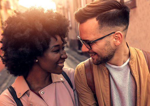 Portrait Of Smiling Couple Looking At Each Other As They Walk Down The City Street.