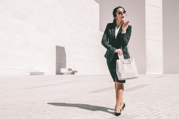 Happy playful businesswoman blowing kiss. Young woman in formal suit walking outdoors and putting...