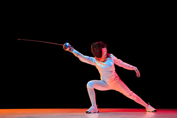 Forward. Teen girl in fencing costume with sword in hand isolated on black background, neon light....