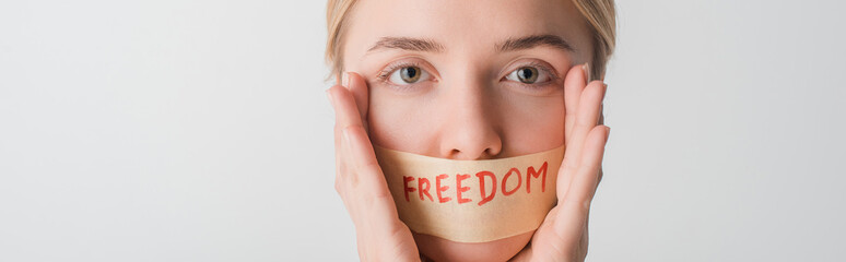 panoramic shot of woman with scotch tape on mouth with freedom lettering isolated on white, human...
