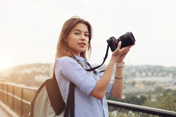 Female photographer came to Europe. Lady walking on street and making photos of sights using professional camera. Cute girl wearing backpack behind