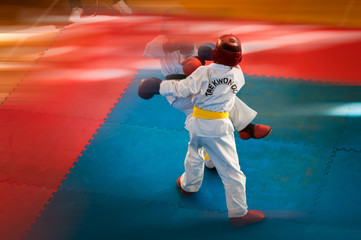 Martial Arts - Taekwondo.  Kids in traditional kimano, hard hats and gloves. Sports duel. For atmospheric, a motion blur film noise effect has been added. Text: Taekwondo is the name for martial art.