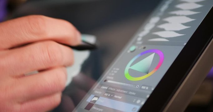 A freelance digital artist or designer picking a color hue and painting with a drawing graphic tablet and pen in an art studio.