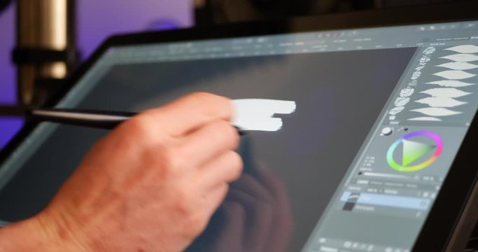 A digital artist selecting a color hue and painting with a drawing graphic tablet and pen in an art studio.