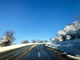 Beautiful winter road view between snow covered trees and sun on the top