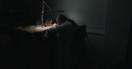 A professional watchmaker working through the night repairing - wide shot