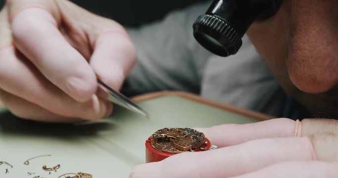 A watchmaker carefully unscrewing the parts of a watch to repair it - Close up