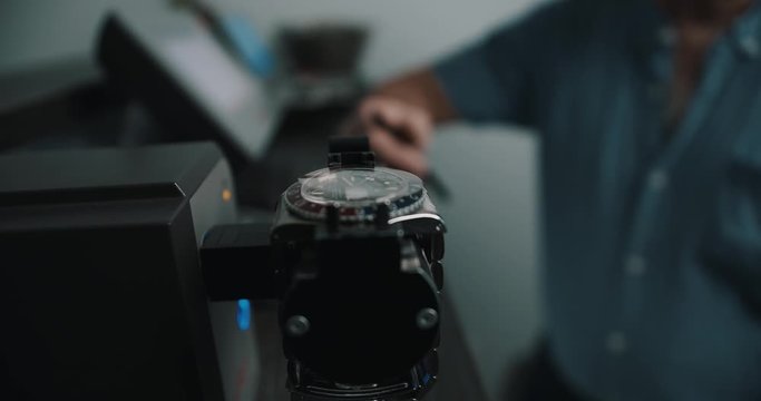A watchmaker waiting in the background for the timegrapher to compete it's reading for the watch - close up
